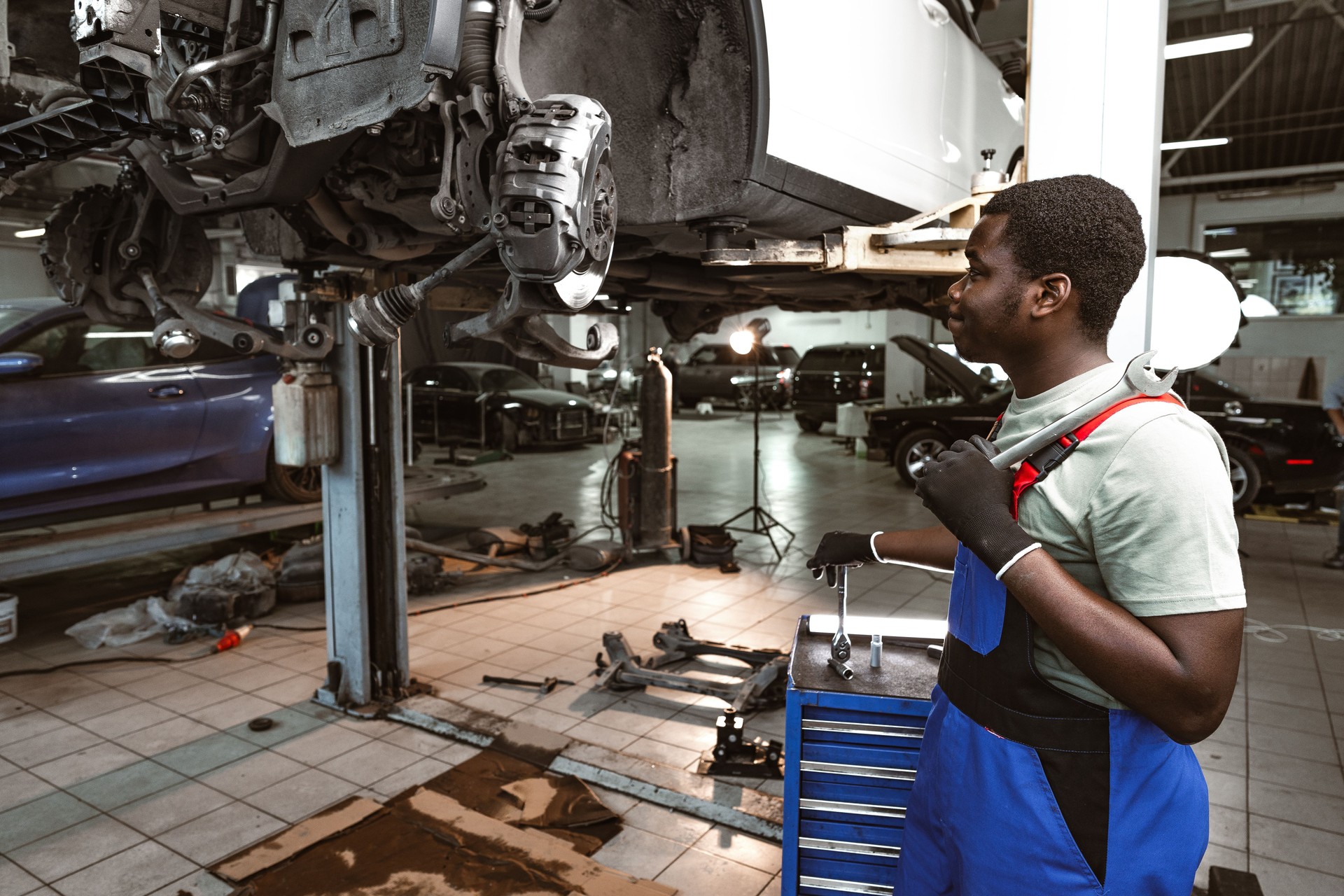 African male auto-mechanic repairing car brakes under the car in auto service