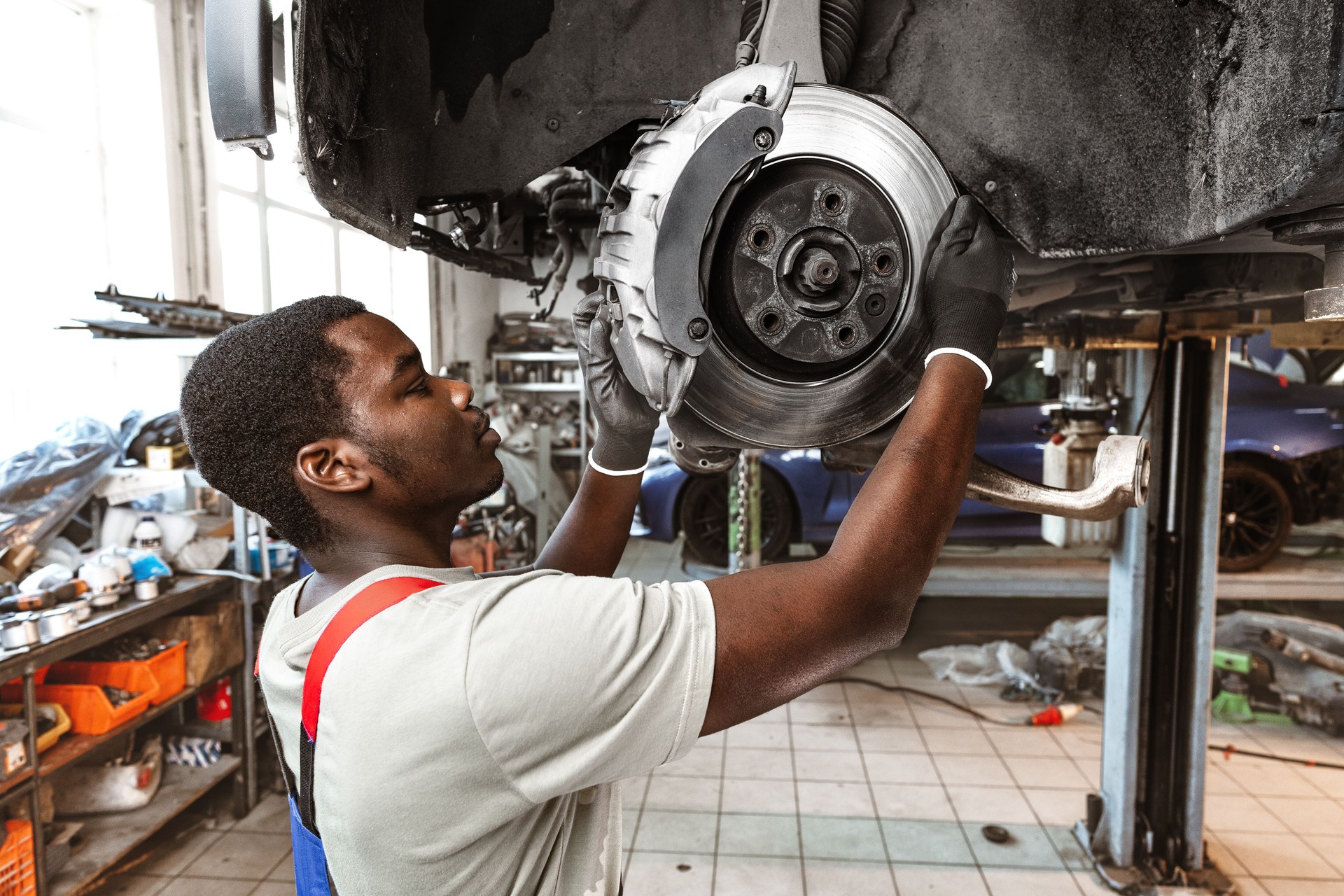 African male auto-mechanic repairing car brakes under the car in auto service